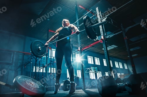 Preview: Fit young woman lifting barbells working out in a gym