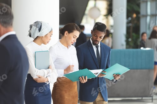 Preview: Front view of young diverse business people looking and discussing business files in lobby