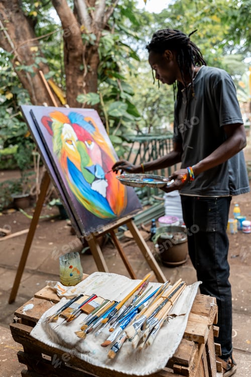 Preview: African rastaman painting a multicolored picture in a patio