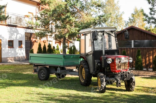 Preview: Modern tractor with empty trailer on green lawn outdoors