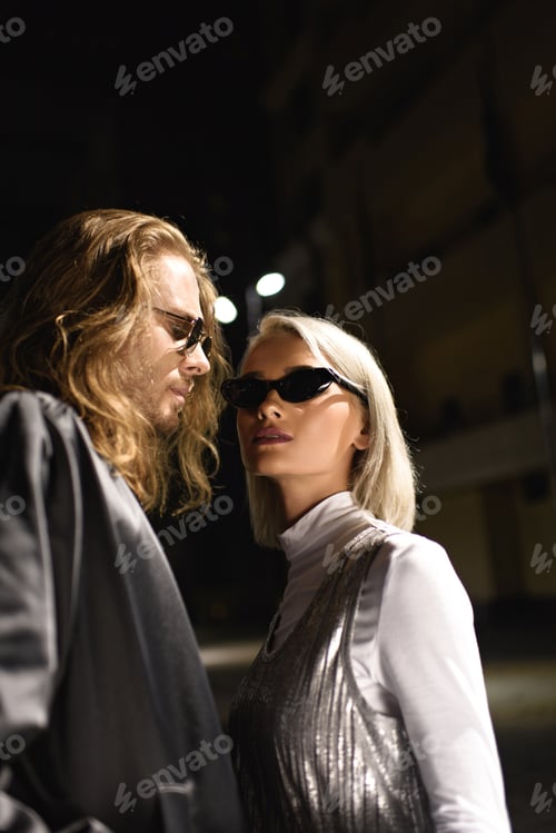 Preview: young fashionable couple in sunglasses flirting on street at night