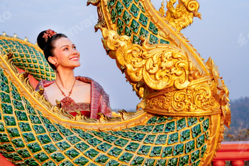 Preview: Close up beautiful Asian woman with Thai traditional dress stand behide the naga sculpture