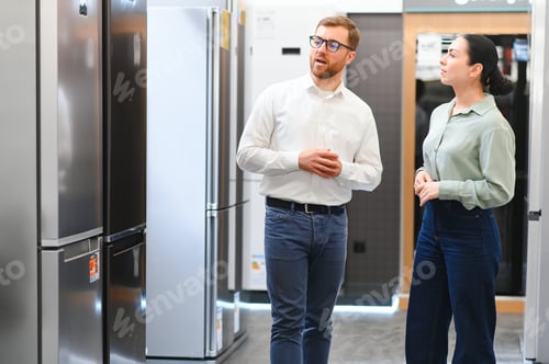 Preview: shop assistant demonstrates refrigerator to young woman in home appliance shopping mall supermarket