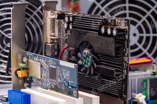 Preview: fragment of computer circuit board with components on the background of power supply fans