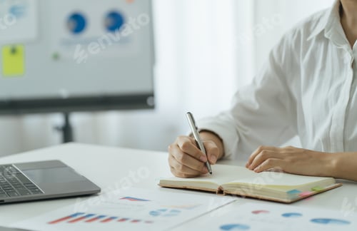 Preview: Business women write on notepad with pen to calculate financial statements within the office.