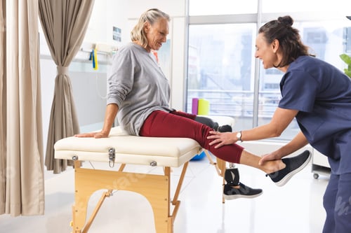 Preview: Caucasian female physiotherapist and senior woman with artificial leg stretching at hospital