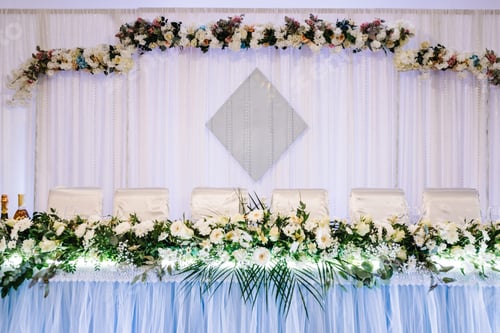 Preview: Festive table with arch decorated composition of white flowers and greenery in the banquet hall.