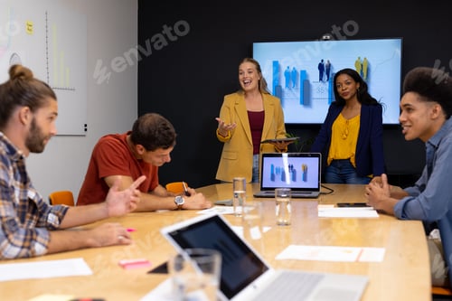 Preview: Happy diverse creative colleagues with laptops and notes discussing project in meeting room