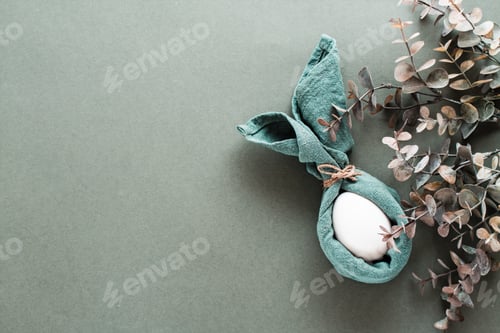 Preview: A white chicken egg is wrapped in a napkin in the form of a rabbit and a branch of eucalyptus
