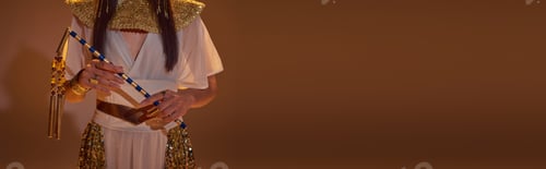 Preview: Cropped view of woman in elegant egyptian look holding flail on brown background, banner