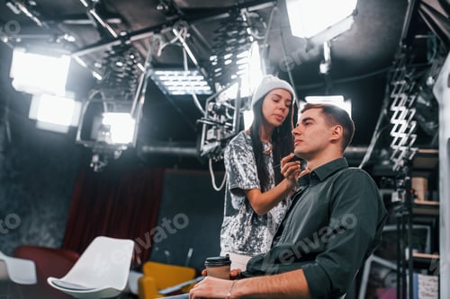 Preview: Young man is preparing for TV online broadcast. Woman helps with make up