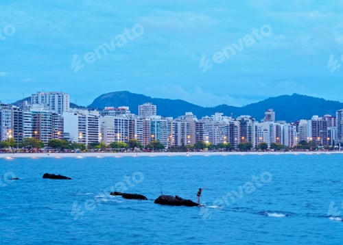 Preview: Coastal Serenity: person on rocks with city skyline