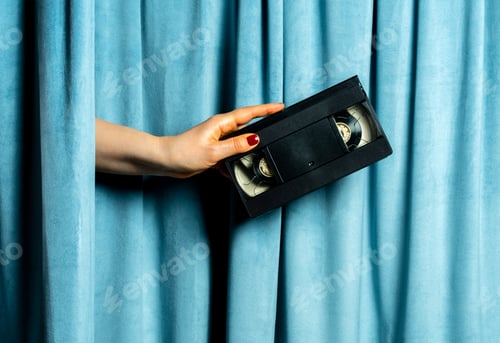 Preview: Female hand holds video tape against blue velvet curtains