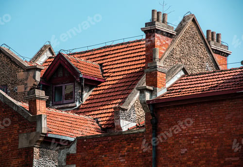 Preview: Old building's red brick and tiled roof with chimneys under blue sky