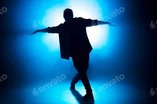 Preview: Sporty modern style hip-hop dancer shows his dance on blue studio background.