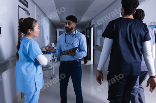 Preview: Diverse male and female doctors talking and using tablet in hospital corridor