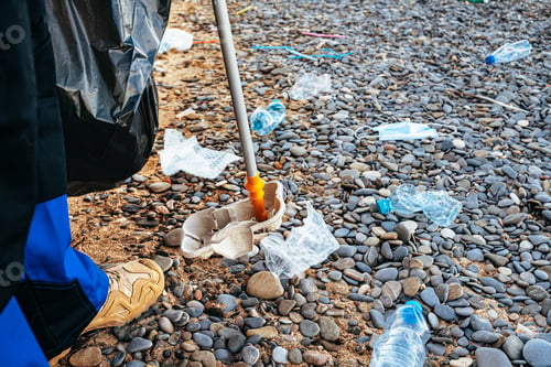 Preview: Close up photo of a man collecting garbage with a grabbing tool on the beach