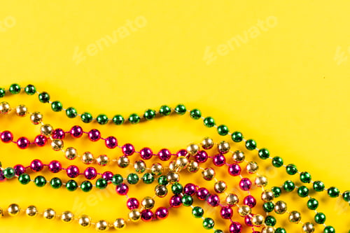 Preview: Composition of colourful mardi gras beads on yellow background with copy space