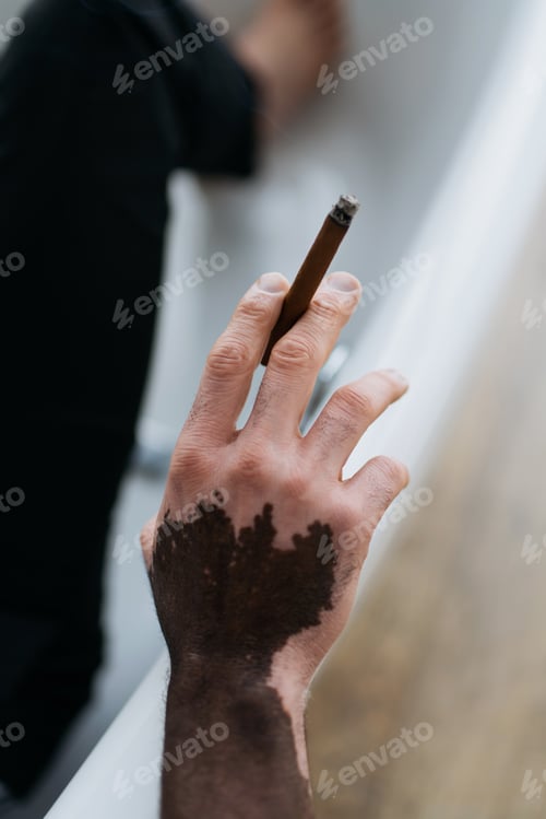 Preview: Cropped view of african american man with vitiligo holding cigar in bathtub at home