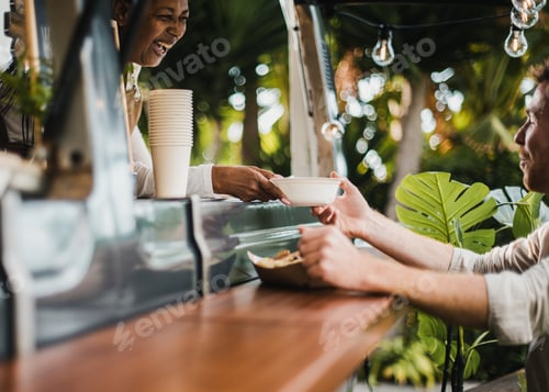 Preview: Senior african woman serving food to customer inside food truck - Focus on hands holding food plate