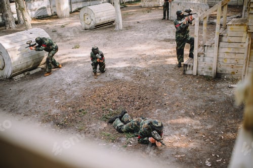 Preview: high angle view of paintball team in uniform and protective masks playing paintball with markers