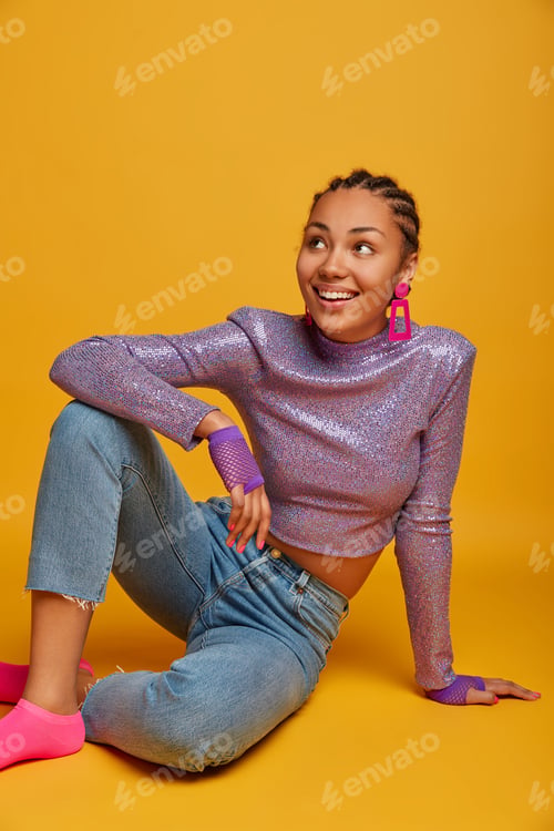 Preview: Studio shot of beautiful cheerful woman sits relaxed on floor and looks aside happily, feels pleased