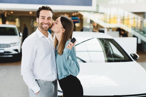 Preview: Wife kissing her husband after buying purchasing giving new car at automobile dealer shop store