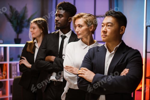 Visualização: Equipe de negócios em trajes formais está olhando para longe enquanto está em uma fileira com os braços cruzados no escritório