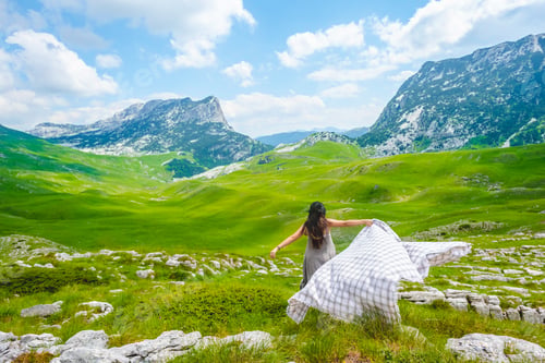 Preview: back view of woman running on valley with blanket in Durmitor massif, Montenegro