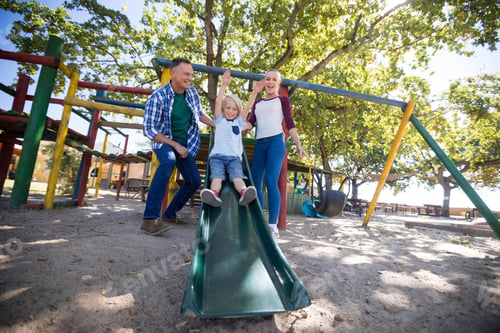 Preview: Happy parents looking at son sliding at playground