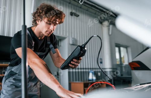 Preview: Tests car's electronics. Adult man in grey colored uniform works in the automobile salon