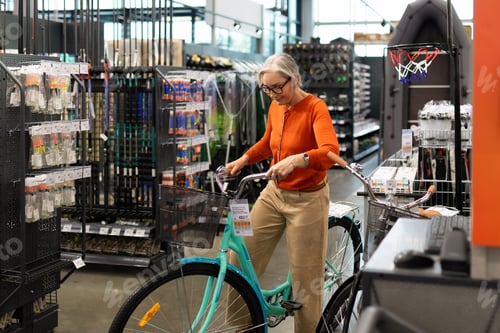 Preview: Senior woman shops for a bicycle in a well-stocked sporting goods store during daytime
