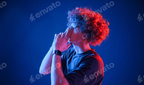 Preview: Young man with curly hair is indoors illuminated by neon lighting
