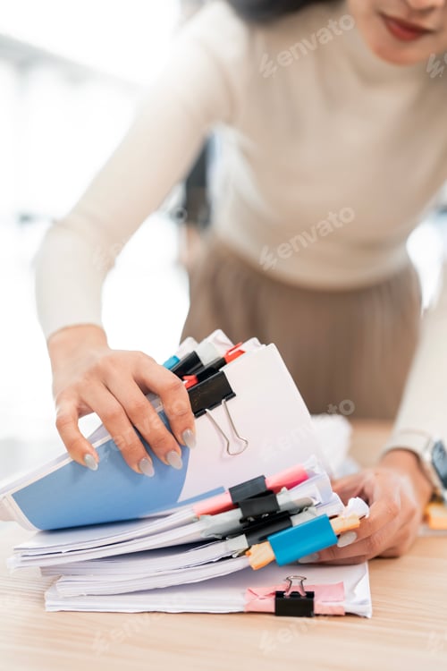 Preview: A close-up shot of a woman organizing a stack of business documents, using colorful binder clips,
