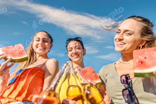 Preview: Happy friends women toasting and drinking bottled beer to the sea at sunset