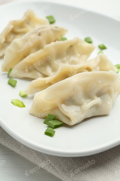 Preview: Tasty boiled gyoza (dumplings) with green onion on white table, closeup