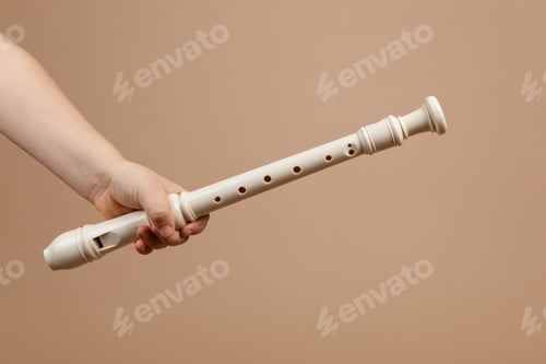Preview: Hold ivory color common fipple flute with one hand closeup, beige background. Woodwind musical