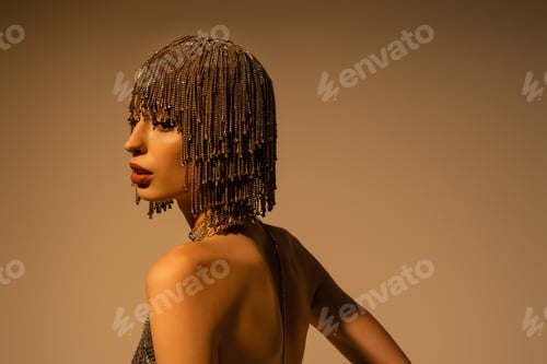 Preview: Pretty woman in top with naked shoulders and jewelry headwear standing on beige