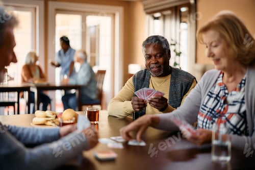 Preview: Happy black senior playing cards with friends in nursing home.