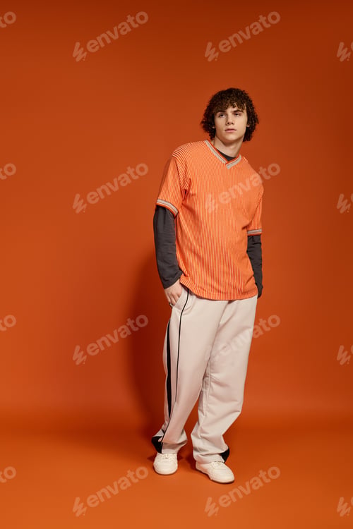 Preview: Teenage boy in casual style poses confidently against a vibrant orange backdrop