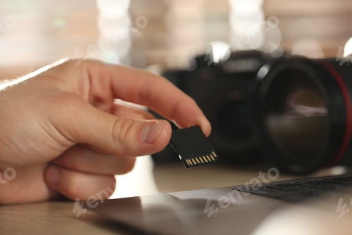 Preview: Man inserting SD memory card into laptop at table indoors, closeup