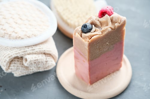 Preview: exfoliating berry and cocoa butter soap bar on a concrete plate and cotton cleansing sponge