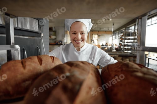 Preview: Portrait of smiling female baker looking through rack with freshly baked breads