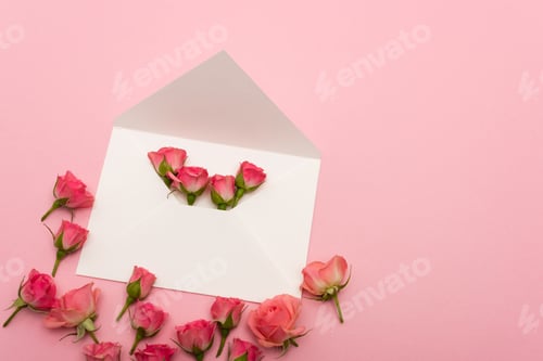 Preview: top view of white envelope with small tea roses isolated on pink