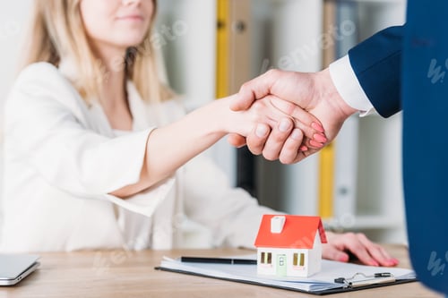 Preview: partial view of smiling woman shaking hands with realtor near house model on table
