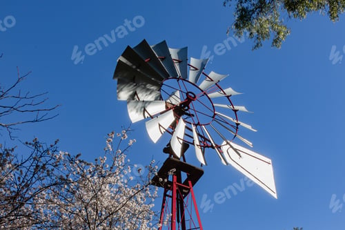 Preview: Low angle shot of a windmill with trees on the foreground under the blue sky