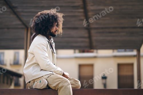 Preview: Young man with afro millennial hair sitting looking thoughtfully side view