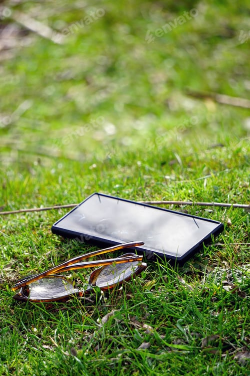 Preview: Smartphone and glasses on a green lawn on a sunny day, vertical