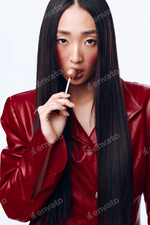 Preview: Stylish woman with long black hair and red leather jacket holding a lollipop on white background