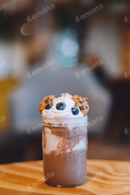 Preview: Vertical closeup of a glassy cup with chocolate milk decorated with cookies and blueberries